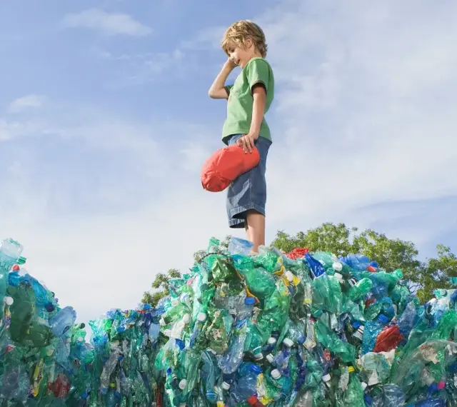 Chłopiec stoi na górze sterty plastikowych butelek, zastanawiając się, co to za pla.