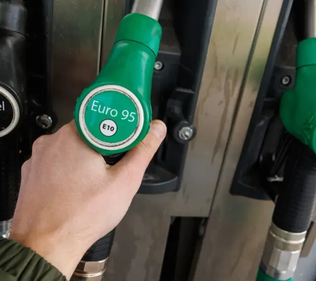 Dłoń trzymająca zielony pistolet z napisem "Euro 95 E10" przy dystrybutorze paliwa. Idealny wybór dla silnika 1.3 multijet.