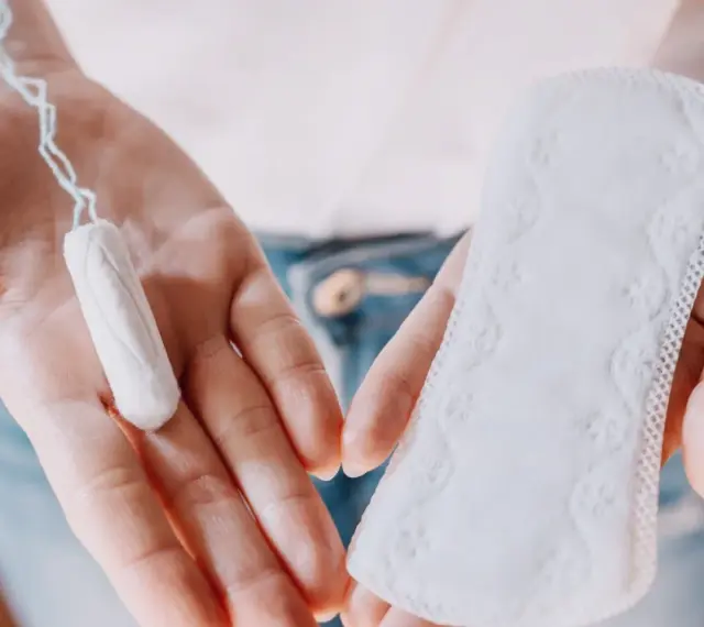 Dłonie trzymają tampon i podpaskę. Czasem pojawia się plamienie zamiast okresu, wtedy wybór jest ważny.