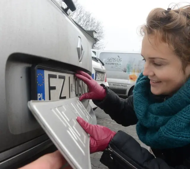 Kobieta w czerwonych rękawiczkach montuje tablicę rejestracyjną.