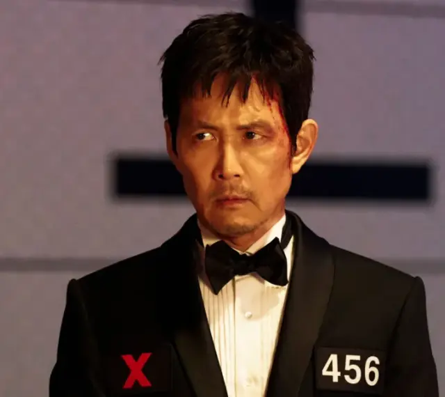 Zraniony Seong Gi-hun w garniturze z numerem 456 i symbolem X, gotowy na kolejne wyzwania w Squid Game sezon 4.