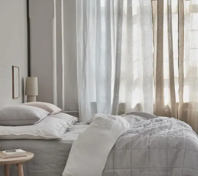 Sanfte Gardinen Ideen für ein Schlafzimmer: Leinenstoffe in Weiß und Beige schaffen eine luftige Atmosphäre über einem gemütlichen Bett.