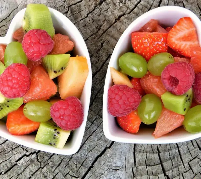 Dwa sercowate talerzyki pełne kolorowych, pokrojonych owoców: truskawek, malin, kiwi, winogron i grejpfruta. Idealne zdrowe przekąski dla dzieci.