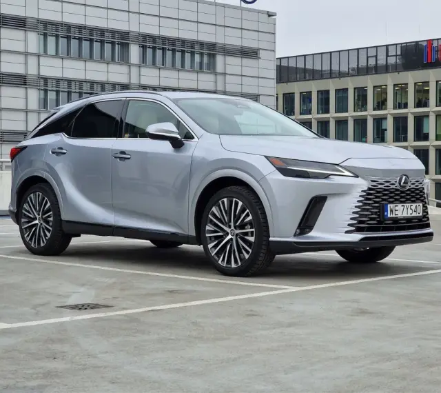 Srebrny Lexus RX 350h zaparkowany przed nowoczesnym budynkiem.