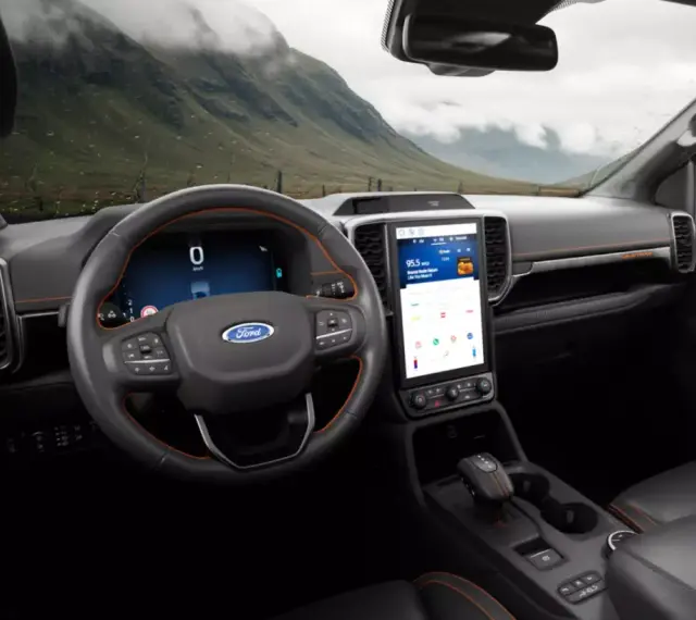 Wnętrze nowoczesnego Ford SUV z dużym ekranem dotykowym i cyfrowymi zegarami. Widok na górzysty krajobraz przez przednią szybę.