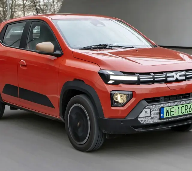 Pomarańczowy Dacia Spring, najtańsze auto elektryczne, jedzie po drodze.