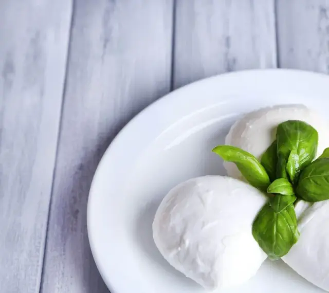 Trzy kulki serka mozzarella z listkami bazylii na białym talerzu. Idealne do sałatki, znasz ser mozzarella kcal?