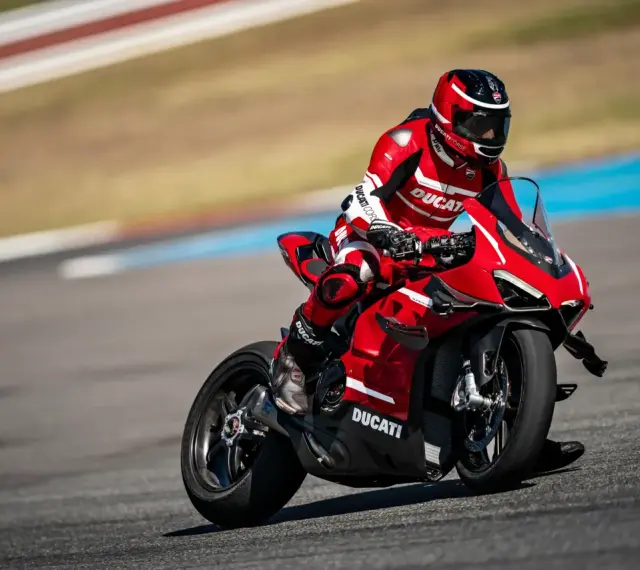 Motocyklista w czerwonym kombinezonie śmiga na torze wyścigowym na swoim czerwonym Ducati Panigale V4.
