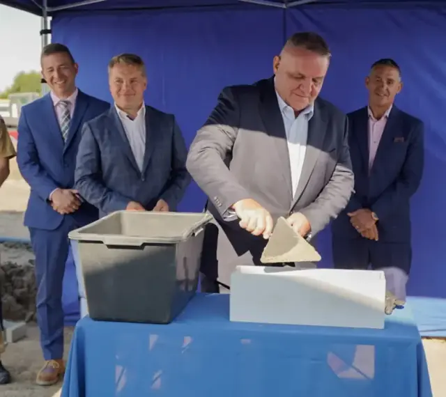 Uroczyste wmurowanie kamienia węgielnego. Mężczyzna w garniturze z kielnią w dłoni symbolicznie rozpoczyna budowę.