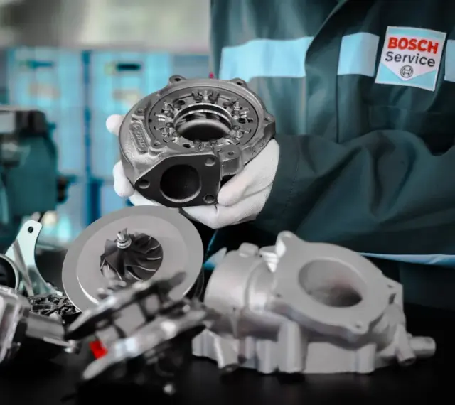 Mechanik w białych rękawiczkach prezentuje części turbosprężarki, sugerując domowe ustawienie sztangi turbiny.