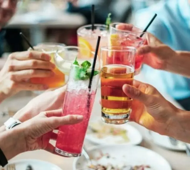Ludzie wznoszą toasty kolorowymi drinkami. Zastanawiasz się, ile alkoholu można wziąć do Norwegii?