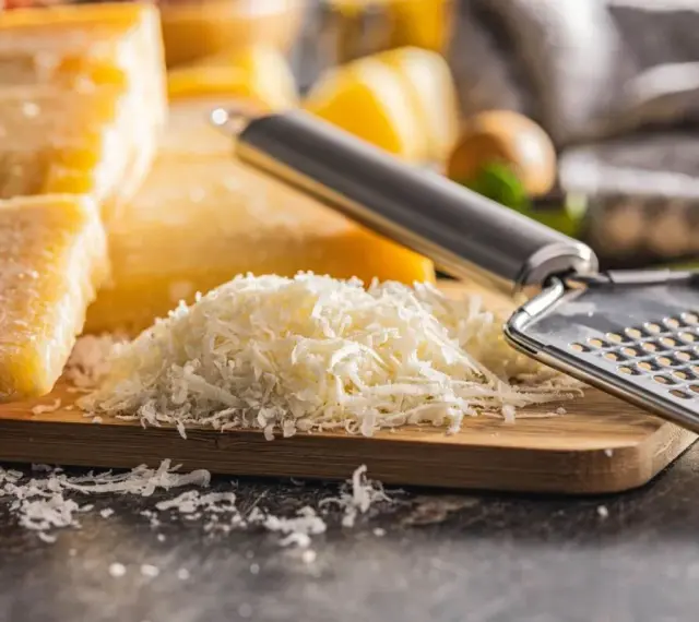 Stos tartego parmezanu, znanego jako parmigiano reggiano, obok bloków sera i tarki.