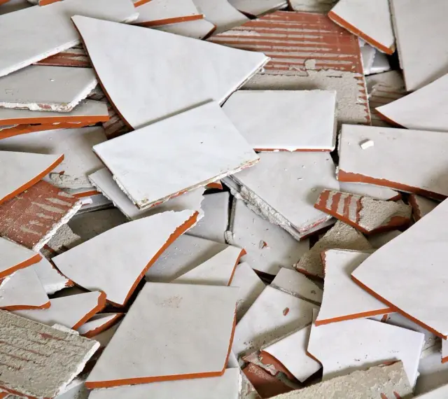 Stos białych, połamanych płytek ceramicznych z pomarańczowymi krawędziami. Wskazówka, jak zdjąć płytki ze ściany bez uszkodzenia.