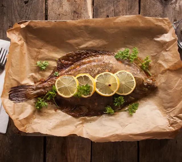 Gebackene Scholle mit Zitronenscheiben und Petersilie auf Backpapier. Perfekt zum Scholle essen!