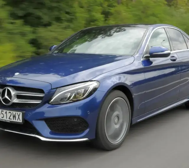 Błękitny Mercedes E220d w ruchu, z rozmytym tłem zieleni i drogi. Elegancki sedan na polskich tablicach rejestracyjnych.