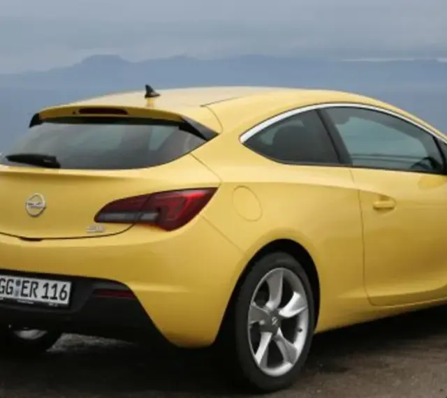 Żółta Astra GTC z tablicą rejestracyjną GG ER 116 stoi na tle morza i gór.