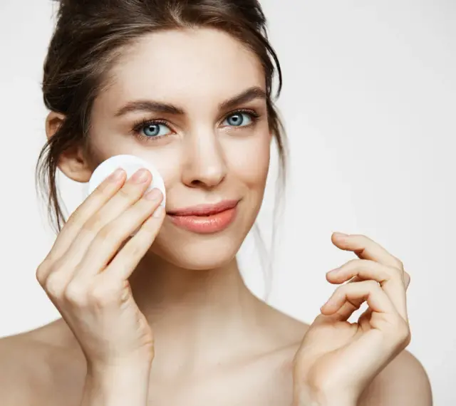 Kobieta z niebieskimi oczami delikatnie przeciera twarz wacikiem. Poznaj sekret, jak rozjaśnić twarz i uzyskać promienny wygląd.