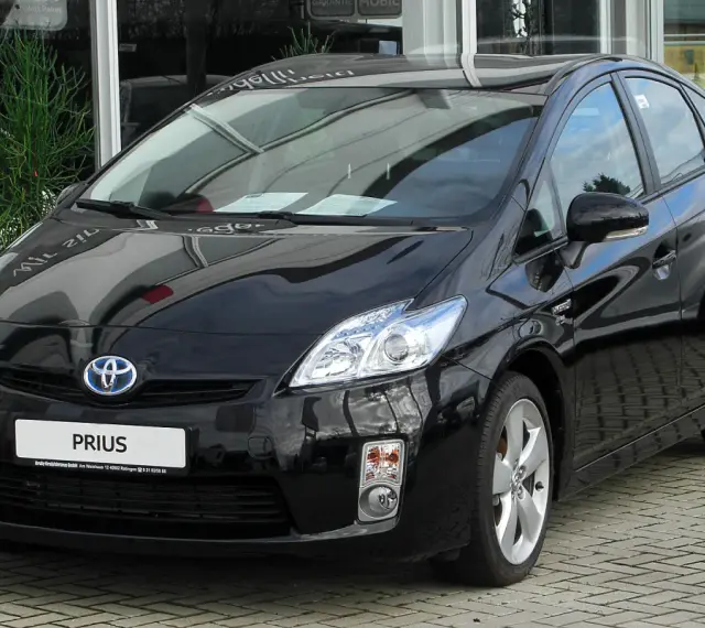 Czarny Toyota Prius 3, hybrydowy samochód, lśni na tle salonu samochodowego.