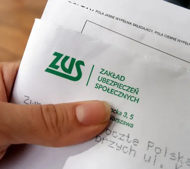 Dłoń trzyma dokument z logo ZUS i napisem "Zakład Ubezpieczeń Społecznych".