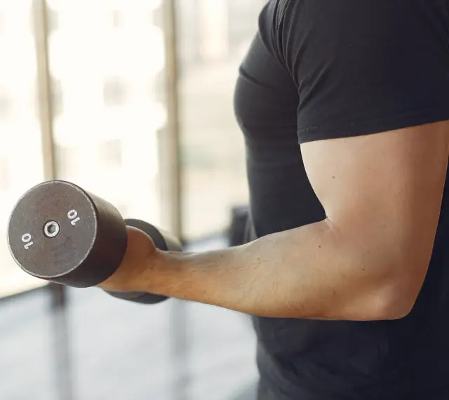 Mężczyzna w czarnej koszulce wykonuje ćwiczenia na biceps z hantlem 10 kg. To jedne z najlepszych ćwiczeń na biceps.