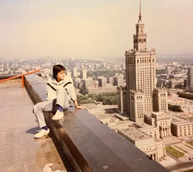 Młody mężczyzna siedzi na dachu, patrząc na panoramę Warszawy. W tle Pałac Kultury i Nauki, który wtedy był najwyższym budynkiem, zanim powstał Marriott.