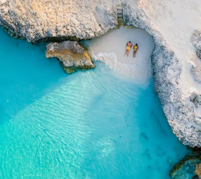 Para na plaży na wyspie Aruba, otoczonej turkusową wodą i skalistymi klifami. Idealne miejsce na relaks.