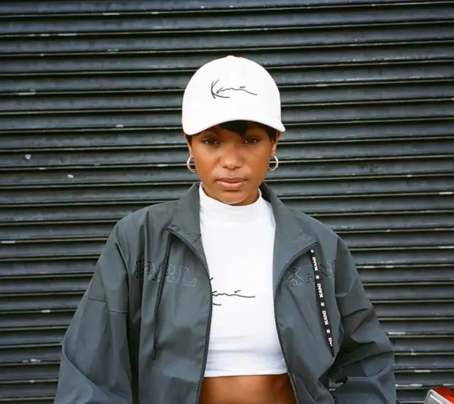 Kobieta w białej czapce z logo Karl Kani i kurtce tej marki. To kultowa marka streetwearowa.