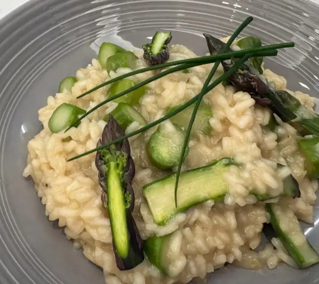 Kremowe risotto z zielonymi szparagami i szczypiorkiem na szarym talerzu.