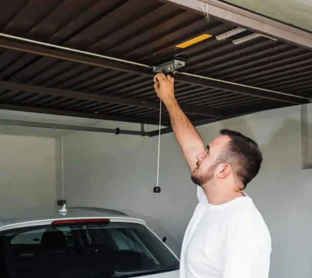 Mężczyzna sprawdza mechanizm bramy garażowej. Czy warto inwestować w garaże i miejsca postojowe przy obecnych cenach najmu?