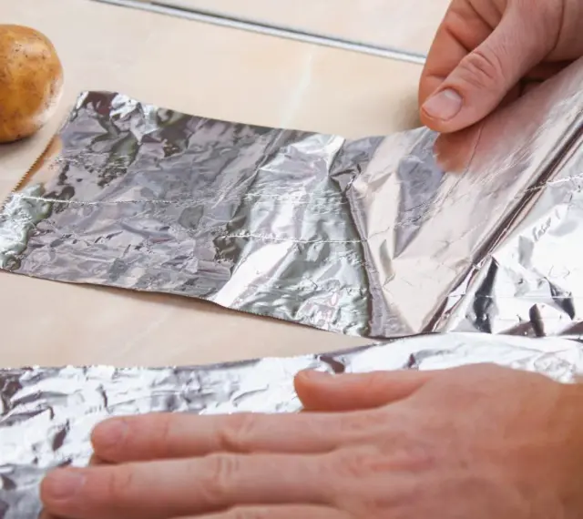 Ręce rozwijają folię aluminiową obok ziemniaków. Zastanawiasz się, gdzie wyrzucić folię aluminiową?