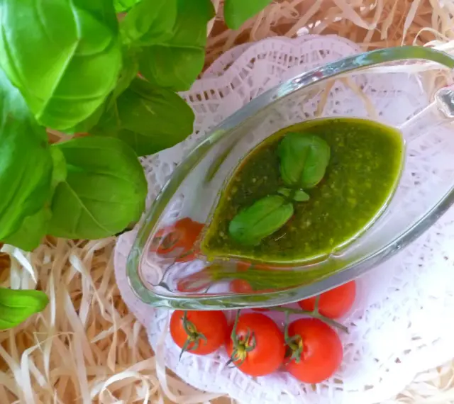 Świeże liście bazylii i pomidorki koktajlowe obok sosu pesto z bazylii w szklanym naczyniu.