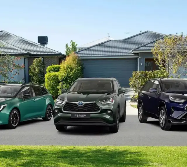 Trzy modele Toyota SUV: zielony kombi, ciemnozielony Highlander Hybrid i granatowy RAV4 Plug-in Hybrid, zaparkowane przed domami.