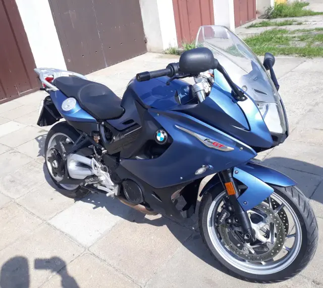 Błękitny motocykl BMW F800 GT stoi na chodniku przed garażem.