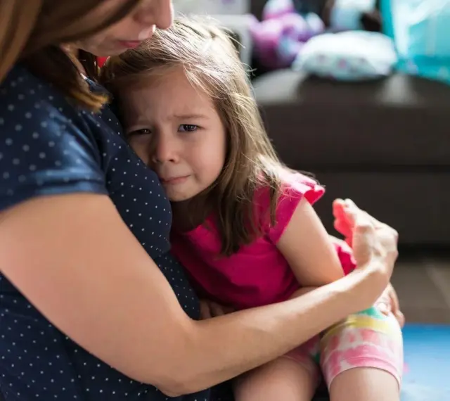 Mała dziewczynka płacze, wtulona w mamę. To właśnie parenting – trudne chwile i bezwarunkowa miłość.