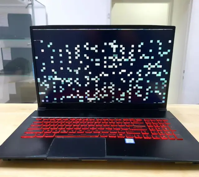 Laptop z artefaktami na ekranie, wskazującymi na problemy z kartą graficzną. Klawiatura podświetlona na czerwono.