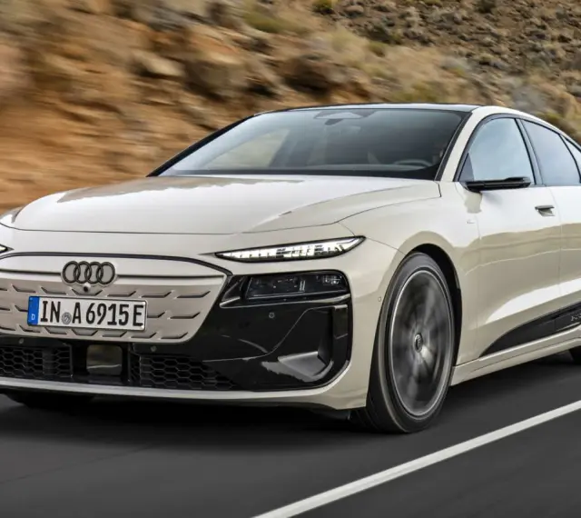 Jasnoszary Audi A6 e-tron z czarnymi akcentami jedzie po drodze.