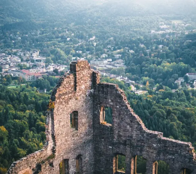 Ruinen einer Burg mit Blick auf eine Stadt und bewaldete Hügel.