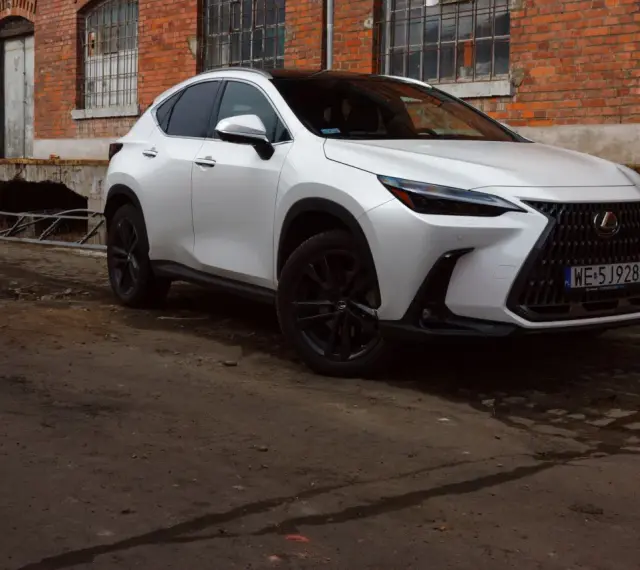 Biały Lexus 350h z czarnymi felgami stoi przed starą ceglaną budowką.