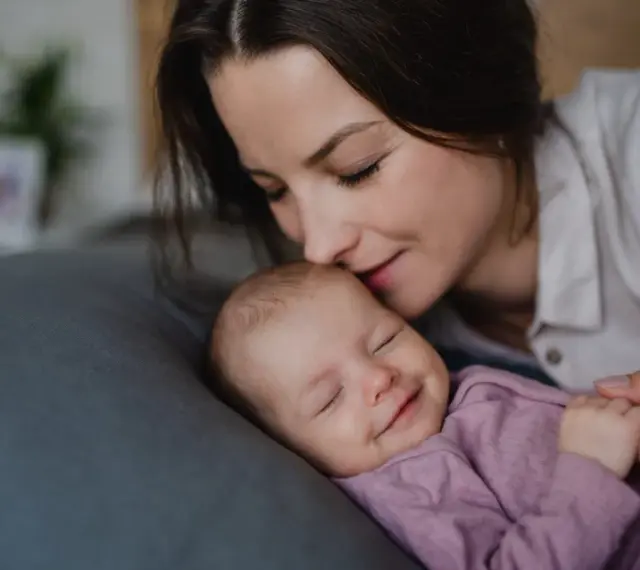 Mama całuje śpiące dziecko. Wkrótce wybierzemy dla niej słodkie imiona dla dziewczynki.