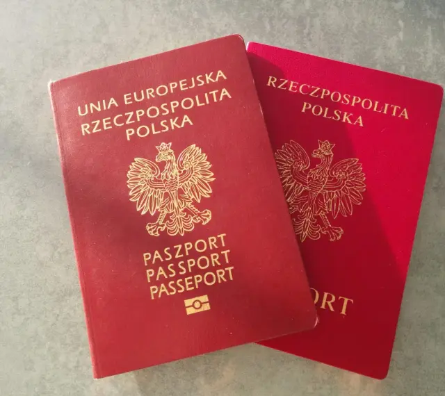 Dwa polskie paszporty w kolorze czerwonym leżą obok siebie na szarym tle.