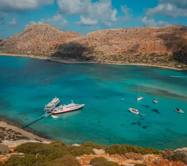 Wycieczka na Santorini z Krety: statki cumują w turkusowej zatoce, otoczonej skalistymi wzgórzami.