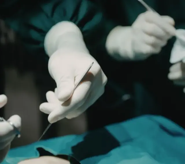 Dłonie chirurga w rękawiczkach trzymające narzędzia chirurgiczne i gazę.