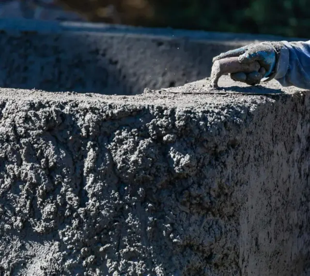 Ręka w rękawicy wygładza świeży beton. Zastanawiasz się, ile kosztuje worek cementu na budowie?