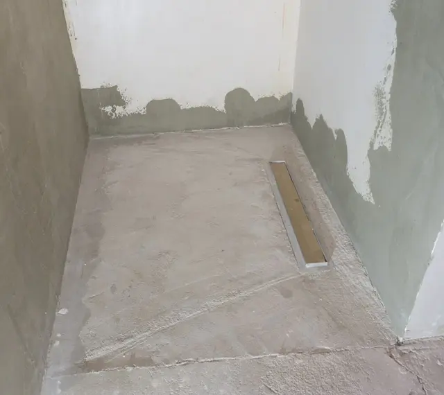 Niedawno położony szlam mineralny w łazience, z widocznym odpływem liniowym. Ściany w trakcie tynkowania.