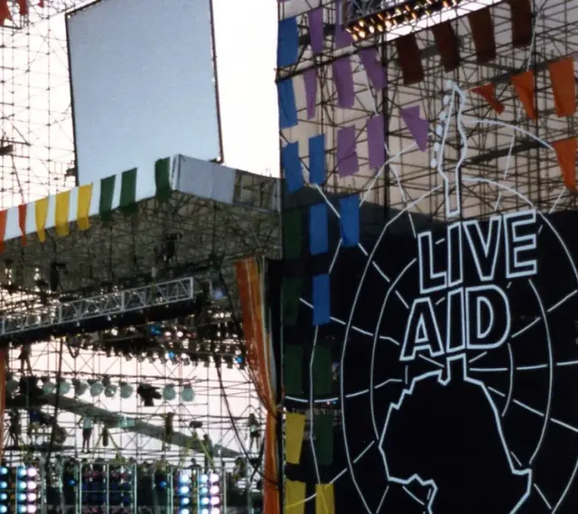 Scena Live Aid w Polsce, ozdobiona kolorowymi flagami i wielkim logo.