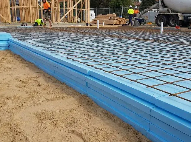 Układanie płyt XPS na fundamentach pod wylewkę betonową. Widoczna siatka zbrojeniowa.