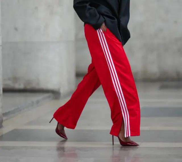 Czerwone spodnie dresowe z białymi lampasami i eleganckie szpilki. Odważne połączenie, które odpowiada na pytanie: jakie buty do dresów?