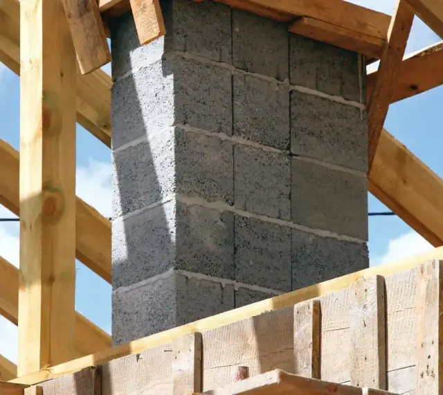 Budowa komina systemowego. Fundament z bloczków betonowych, otoczony drewnianą konstrukcją dachu.