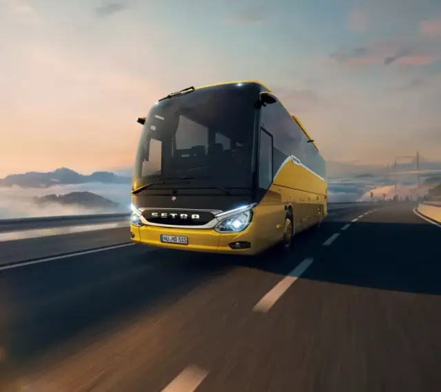 Żółty setra autobus pędzi po autostradzie wśród chmur i gór, w stronę mostu.