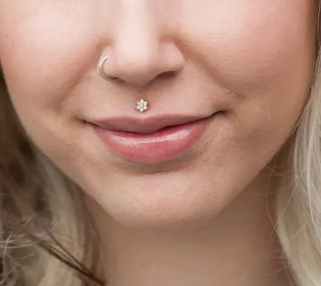 Delikatny labret co to? To ozdoba wargi w kształcie kwiatka z cyrkoniami. Obok kolczyk w nosie.